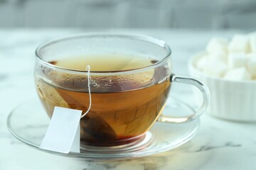 Tea bag in glass cup with hot drink on light marble table, closeup
