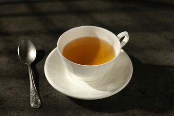 Refreshing green tea in cup and spoon on dark textured table, closeup