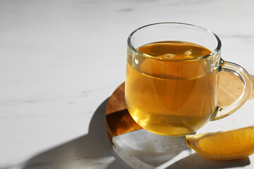 Refreshing green tea in cup and slice of lemon on white marble table, closeup. Space for text