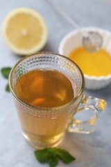 Aromatic mint tea in glass cup, fresh leaves, honey and lemon on light gray table, closeup