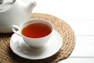 Aromatic black tea in cup and teapot on white wooden table, closeup
