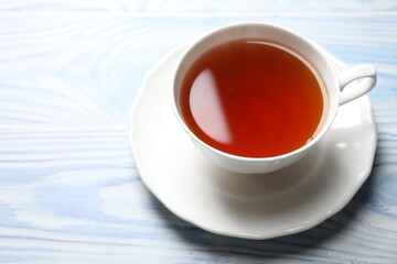 Aromatic black tea in cup on light blue wooden table, closeup. Space for text