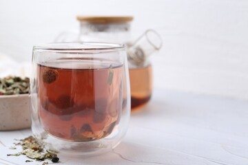 Delicious herbal tea and dry leaves on white table, closeup. Space for text