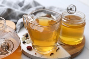 Delicious herbal tea with honey and dry leaves on white table, closeup