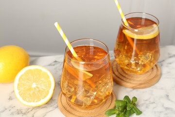 Refreshing iced tea with slices of lemon, mint and drinking straws on white marble table, closeup