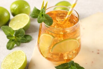 Refreshing iced tea with slices of lime, mint and drinking straw in glass on light table, closeup