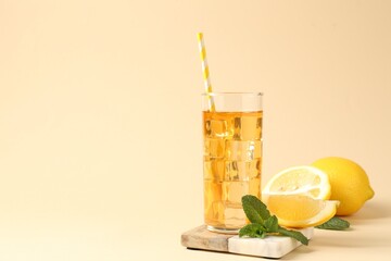Refreshing iced tea with drinking straw in glass, mint and lemon on beige background, closeup. Space for text
