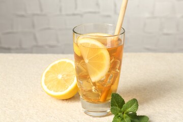 Refreshing iced tea with drinking straw, mint and slices of lemon on light textured table against grey background, closeup