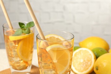 Refreshing iced tea with drinking straws, mint and lemon on light table against grey background, closeup