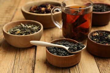 Aromatic tea and dried leaves on wooden table, closeup