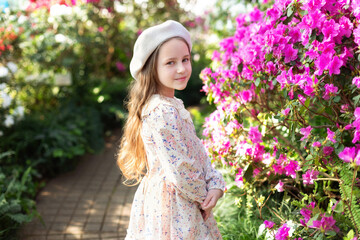Obraz premium Beautiful caucasian little girl in greenhouse among bush colorful azalea flowers. Portrait of a child girl wearing pink dress and wear beret in the botanical garden arbor among the blossom flowers. 