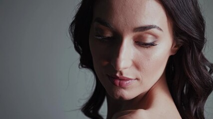 Close-up video still of a woman with soft lighting and a neutral background, captured from a slightly elevated angle, highlighting her expression. - Powered by Adobe