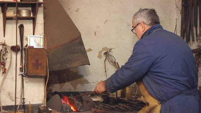 Blacksmith at work, coal fire melts iron in a furnace for further processing with a hammer on an anvil in smithy, close-up. Traditional manual production in the forge, blacksmith workshop