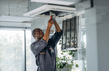High up, fixing the ventilation. Repairman is indoors in the modern office