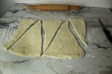 triangles of raw dough on the table, rolling pin, knife. Homemade cakes