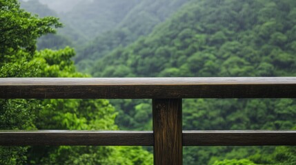 Fototapeta premium Scenic wooden railing overlooking lush green mountains in a misty landscape