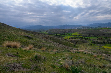 Naklejka premium Rolling green hills under a moody sky with scattered clouds at dusk in a rural landscape