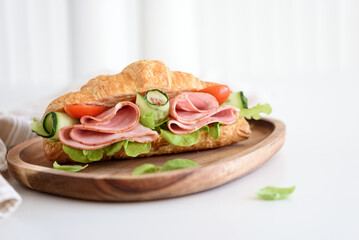 Ham and Cheese Croissant Sandwich on wooden plate on white table. Healthy breakfast.