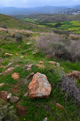 Vibrant green hills with rocky terrain under a cloudy sky in the distance