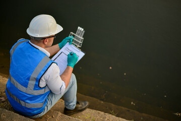 An expert ecologist is taking water samples back to a science lab to test aquatic life to examine...
