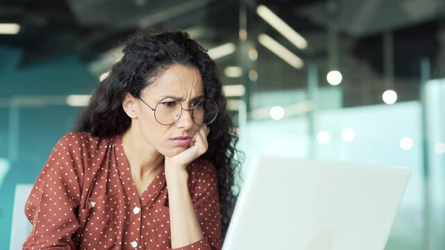 Confused young female employee working on laptop while sitting at desk at a workplace in a modern business office. Disoriented puzzled businesswoman has stress and cannot concentrate on task. Close up