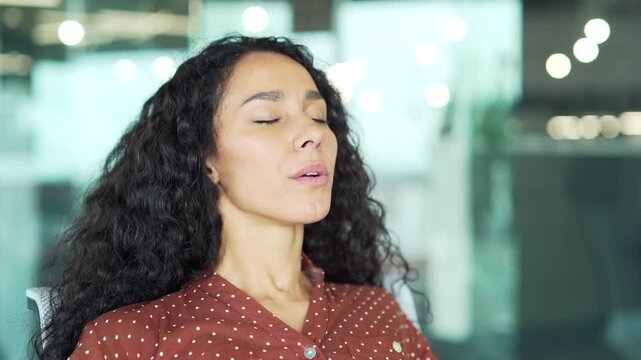 Young businesswoman relaxing breathing deeply while sitting at a workplace in a business office. Calm happy female employee resting with her eyes closed. Joyful woman took a break from work. Close up