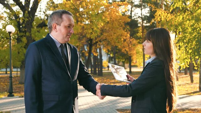 Man and woman discuss potential challenges and risks associated with project. Man and woman propose ways to mitigate risks. Man and woman employees shake hands at end of meeting in park