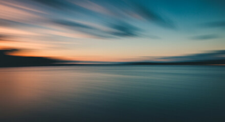 Fototapeta premium Blurred Sunset over Water, Evoking Serenity. A serene, long exposure image of a sunset over water.