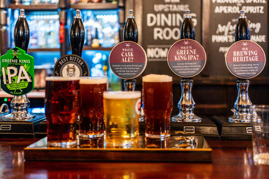 A selection of traditional British ales is served on a wooden tray in a classic London pub. Behind the bar, hand-pulled beer taps display various ale options. London, England