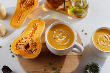 Roasted butternut squash soup with cream and pumpkin seeds on two white mugs.