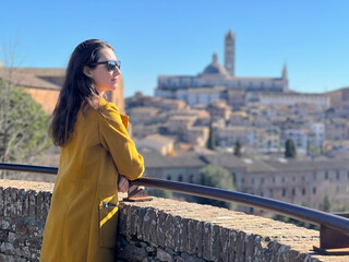 A portrait of a young woman at the background Siena historical city center panorama. Self tourism concept. Travel in Italy in winter