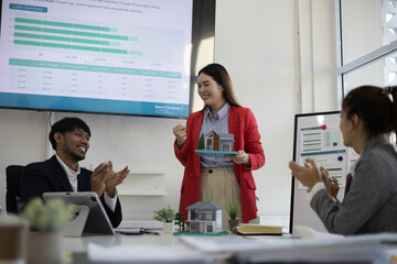 A group of people are sitting around a table with a model house in the middle. They are all smiling and seem to be enjoying themselves
