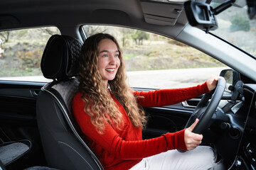 A young white woman driving a car. Side view portrait of a friendly female driver sitting behind...
