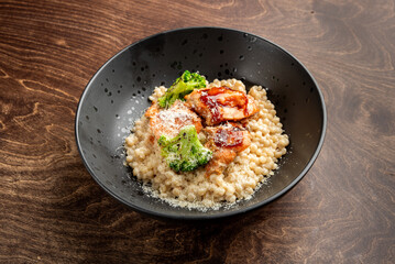 A delicious bowl of creamy risotto topped with grilled salmon, broccoli, and a sprinkle of cheese, served against a rustic wooden background. Perfect for food lovers and culinary presentations.