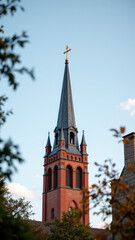 A majestic church with a tall spire reaching into the sky, surrounded by trees under a blue sky.