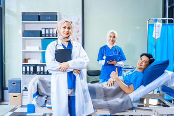 Obraz premium Asian middle-aged man patient rests in a hospital bed while a middle-aged Muslim woman doctor and a middle-aged Asian woman nurse check for diseases like flu and pneumonia, ensuring his recovery.