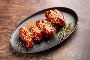 Delicious barbecue chicken wings plated on a dark oval dish, garnished with herbs and a sprinkle of crunchy toppings, showcasing a rich, glistening glaze. Perfect for food photography.