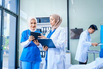 Obraz premium Asian middle-aged man, a middle-aged Muslim woman in hijab, and a middle-aged Asian woman, all medical doctors, work together in a hospital, collaborating with a nurse to provide patient care.