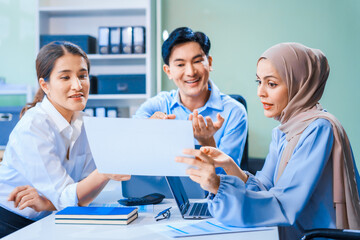 Obraz premium Middle-aged Asian man and Muslim woman in hijab sit across from each other in business meeting. They review report documents, discussing strategies and making decisions, successful, professional.