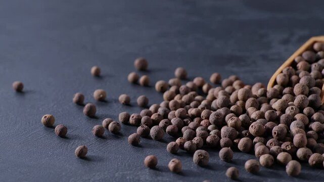 allspice or Jamaican pepper in a wooden serving scoop on a black stone table.
black pepper seeds in a wooden shovel.