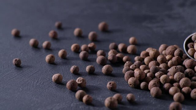 allspice or Jamaican pepper in a measuring spoons on a black stone table.