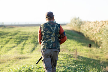 Mature hunter man holding a shotgun and walking through a field