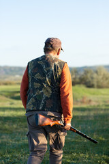 Mature hunter man holding a shotgun and walking through a field