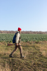 Mature hunter man holding a shotgun and walking through a field