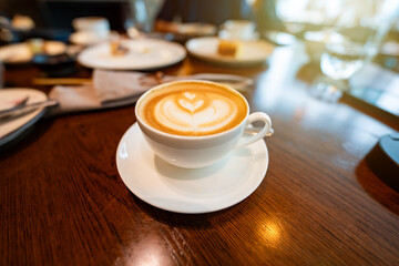 A hot latte with beautiful foam art sits alongside an English breakfast on a rustic wooden table, ideal for showcasing the comfort and charm of cafes and morning dining.