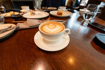 A hot latte with beautiful foam art sits alongside an English breakfast on a rustic wooden table, ideal for showcasing the comfort and charm of cafes and morning dining.