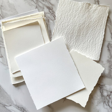 various samples of watercolor paper laid out on a marble surface.  