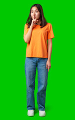 Young woman in orange shirt holding finger to lips on bright green background while signaling to...