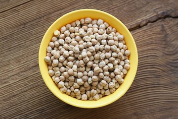 Raw chick peas in an yellow plastic bowl, flat lay. Chick pea on an old wood table.
