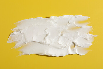 Cream on dark yellow background, top view. Sample of cosmetic product